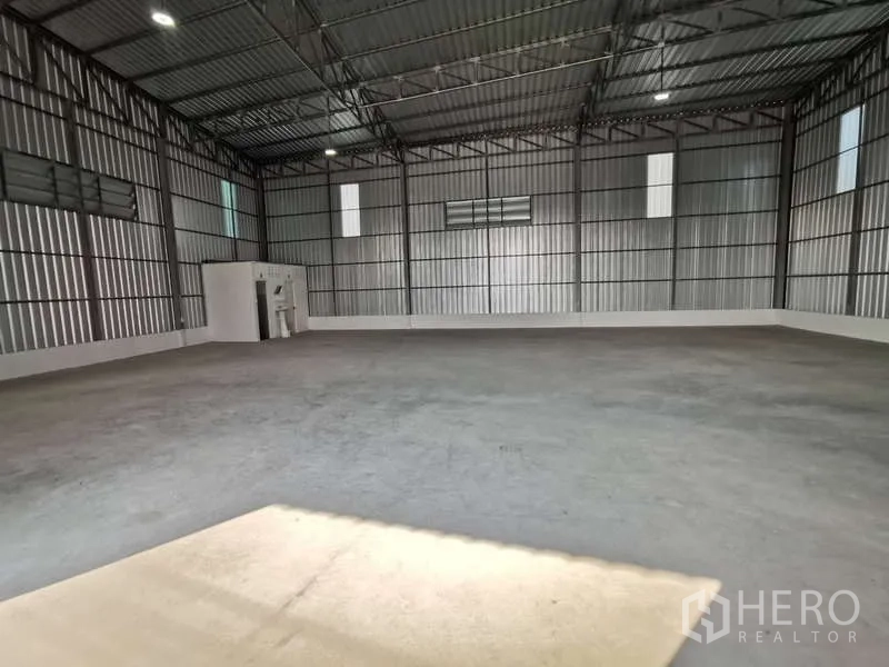 Warehouse for rent in Prawet, Bangkok - Open warehouse space with high ceiling and a corner restroom block under bright lighting.