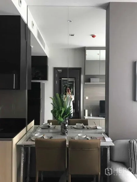 Condominium for rent in Watthana, Bangkok - Dining area with a mirrored wall reflecting the entry and living space, table set for two.