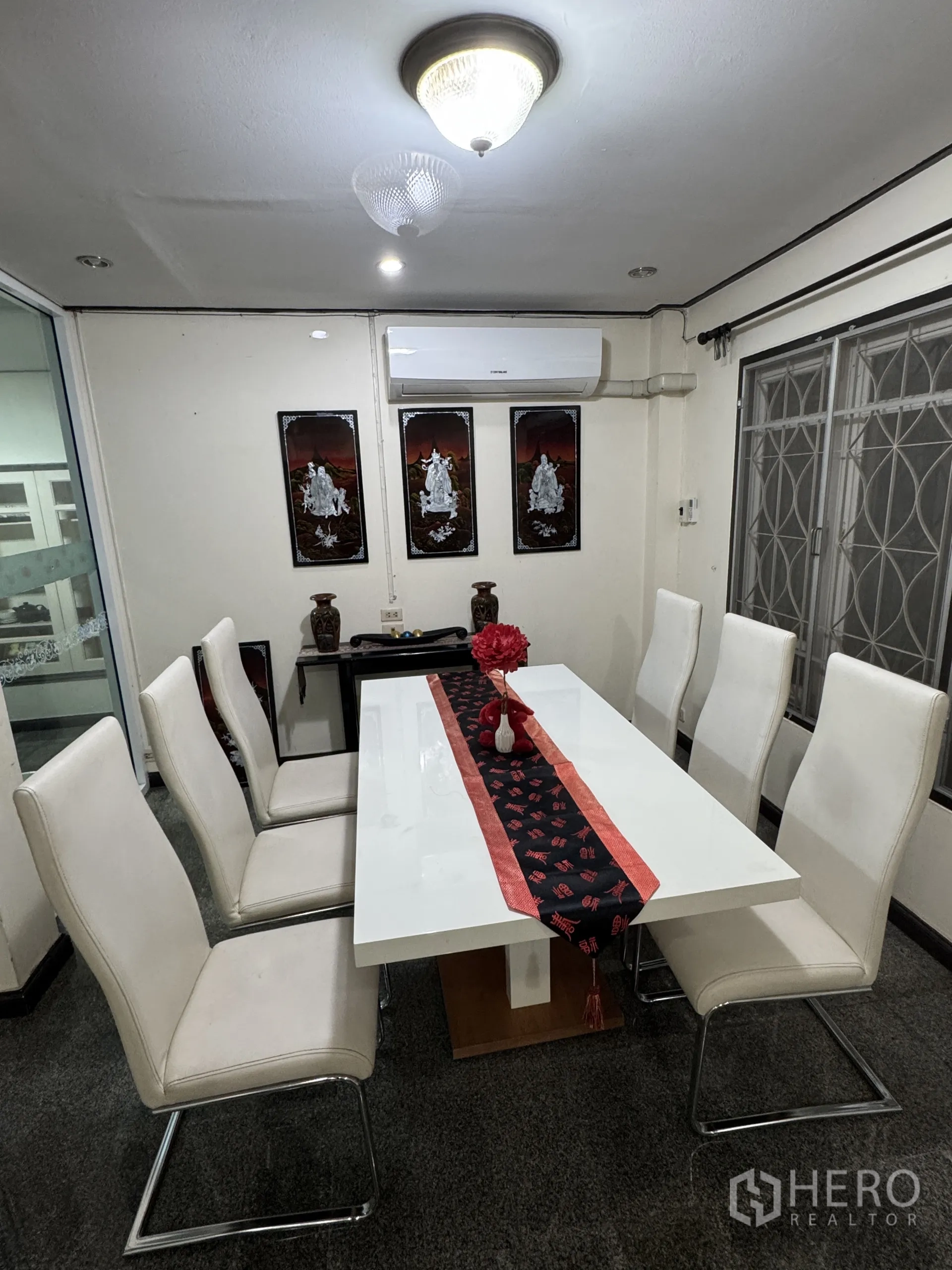 独立式住宅 出租在Min Buri, Bangkok - 餐区配白色八人餐桌、墙面装饰画与空调。