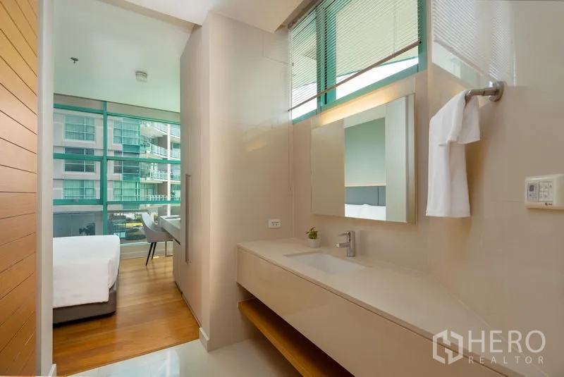Condominium for rent in Bang Kho Laem, Bangkok - Sleek vanity area with a long countertop and mirror connecting to a bedroom with large glass windows.