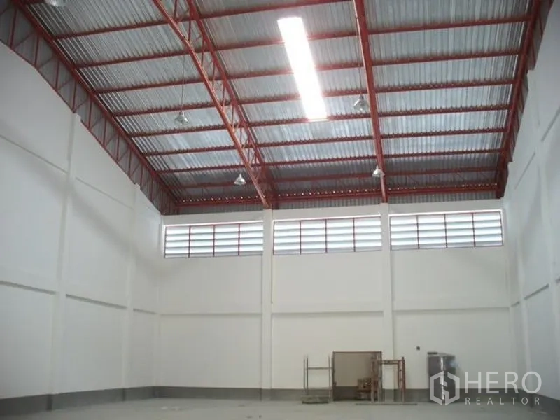 Factory for rent or sale in Samut Prakan - Spacious warehouse interior featuring high red-steel truss roof, clerestory ventilation windows, and bright lighting.