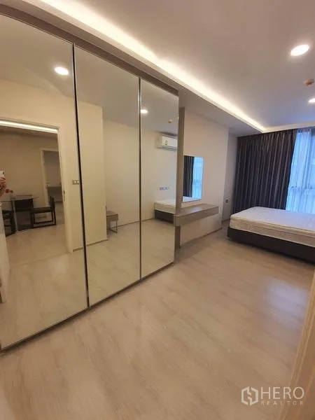 Condominium for rent in Khlong Toei, Bangkok - Second bedroom with mirrored wardrobes, vanity desk and a tall window with curtains.