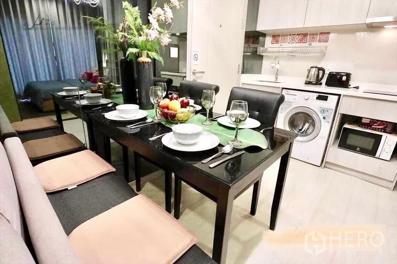Condominium for rent in Khlong Toei, Bangkok - Long black dining table set beside compact kitchen with washer and microwave.