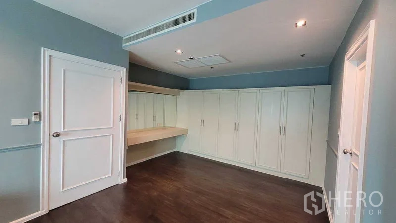 Condominium for rent in Khlong Toei, Bangkok - Spacious master bedroom showing long built-in wardrobes and a dressing desk with mirrors.