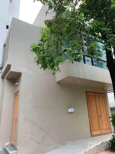 独立式住宅 出租 - 两层现代外立面，木质大门与转角落地窗，门前有树荫。