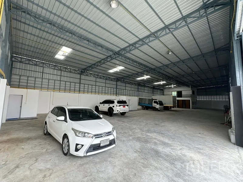 Warehouse for rent in Lam Luk Ka, Pathum Thani - Large clear-span warehouse interior with several vehicles and a durable concrete floor.