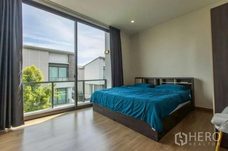 Detached House for rent or sale in Lat Phrao, Bangkok - Bright bedroom with floor-to-ceiling glass opening to a balcony overlooking the neighborhood.