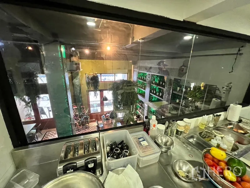 Shophouse for rent in Watthana, Bangkok - View from a prep counter through glass to the dining area with greenery and tall wooden doors.