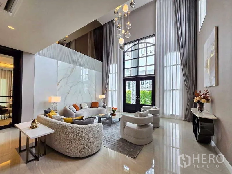 Detached House for rent or sale in Lat Krabang, Bangkok - Living room view to tall arched doors, chandelier, and sheer curtains.