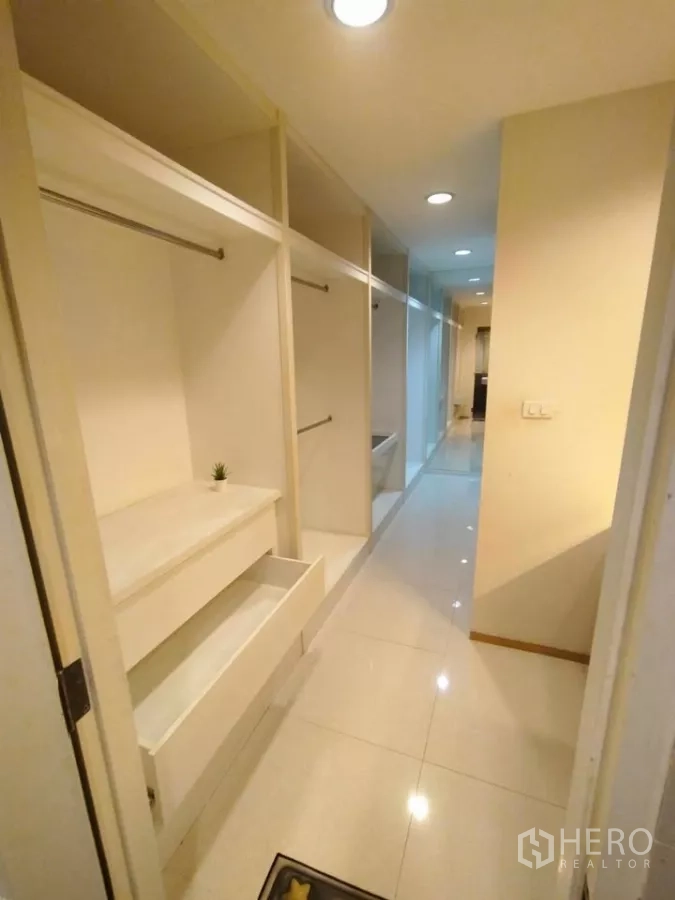 Condominium for rent in Khlong Toei, Bangkok - Walk-in closet corridor with open wardrobes and drawers leading toward the living area.