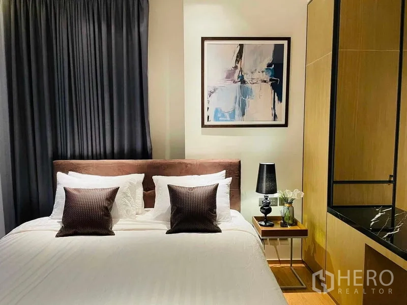 Condominium for rent in Khlong Toei, Bangkok - Cozy bedroom with double bed, artwork, bedside table and warm wood accents.