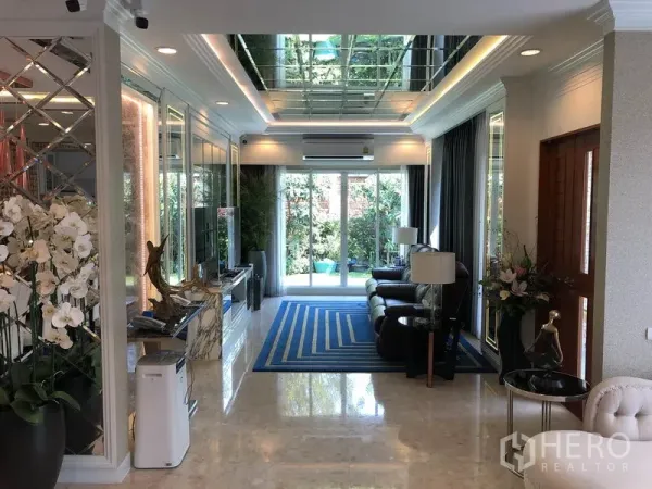 Detached House for rent or sale in Saphan Sung, Bangkok - Elegant living room with mirrored ceiling, marble floors, and glass doors opening to the garden.