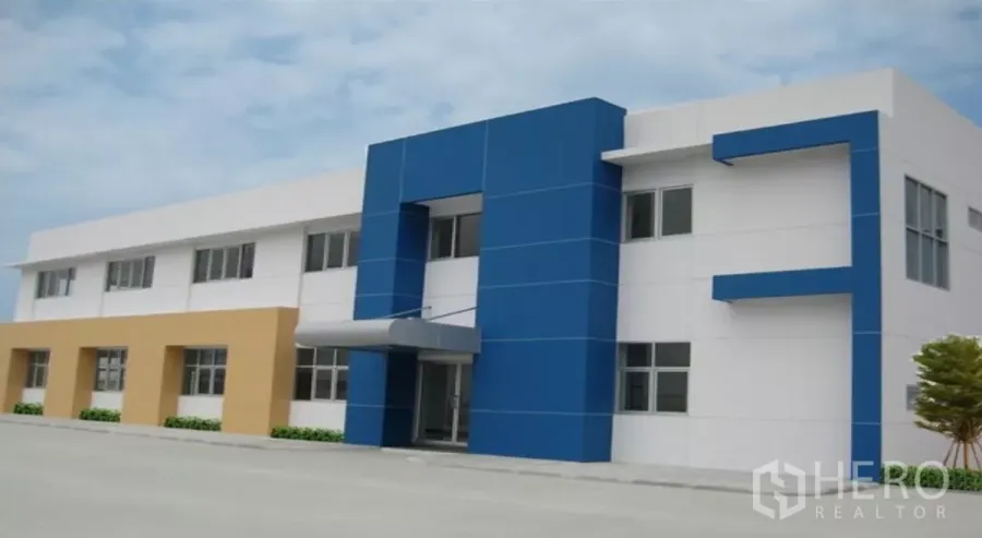 工厂 出租在Chachoengsao - 工业园区内蓝白配色的两层厂房与办公楼，设有门廊入口和宽阔硬化场地。
