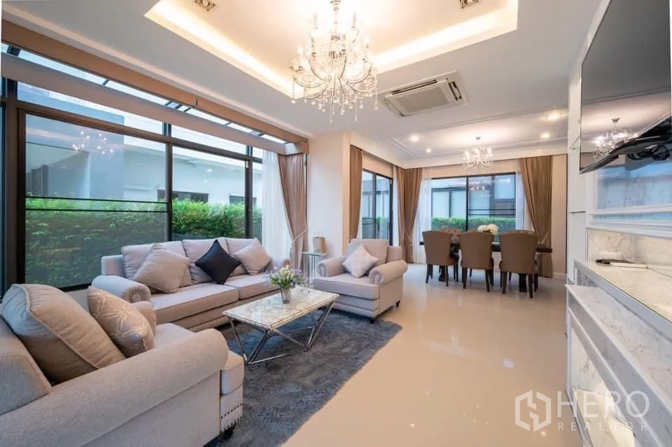 Detached House for rent in Prawet, Bangkok - Living and dining space with floor-to-ceiling windows overlooking hedges.