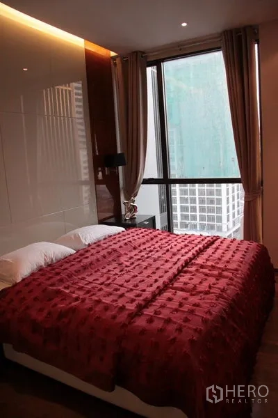 Condominium for rent in Khlong Toei, Bangkok - Bright bedroom with large window, city view, bedside table, and curtains.