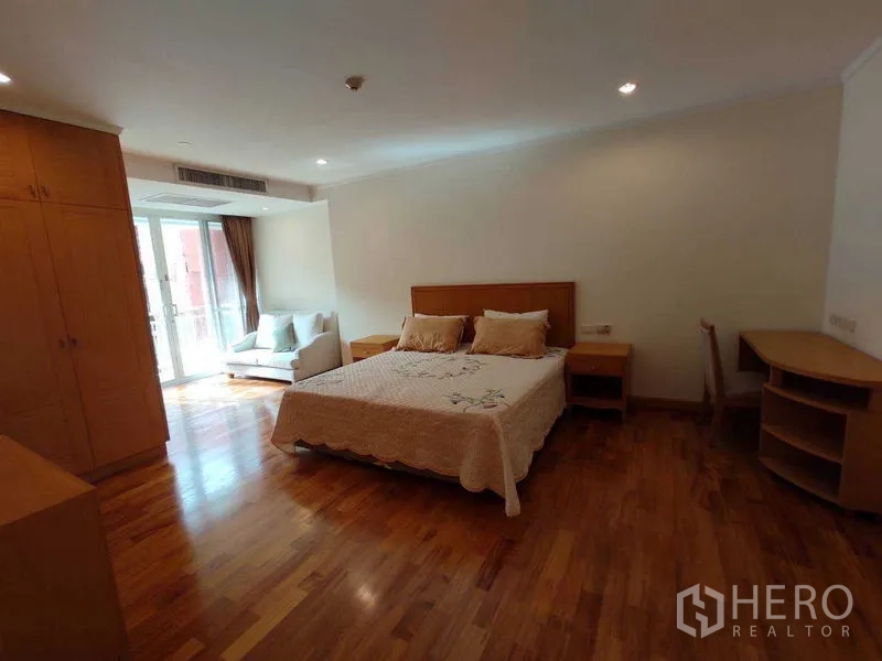 Condominium for rent in Khlong Toei, Bangkok - Large bedroom with bed, study desks, wardrobes and balcony seating area with natural light.