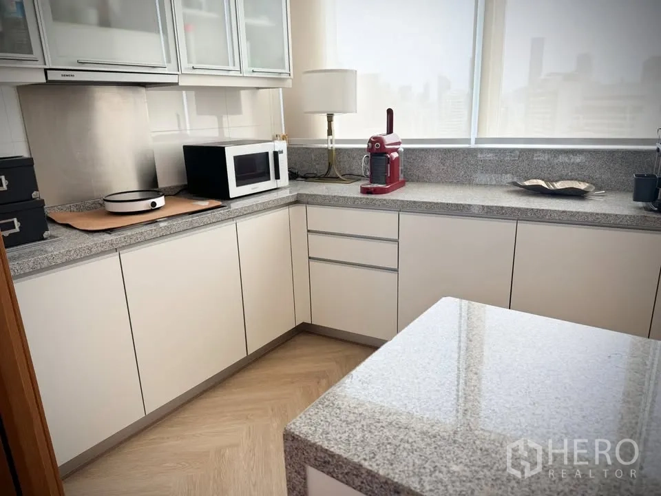 Condominium for rent or sale in Khlong Toei, Bangkok - Bright U-shaped kitchen with granite countertops, white cabinetry, microwave, and a red coffee machine.