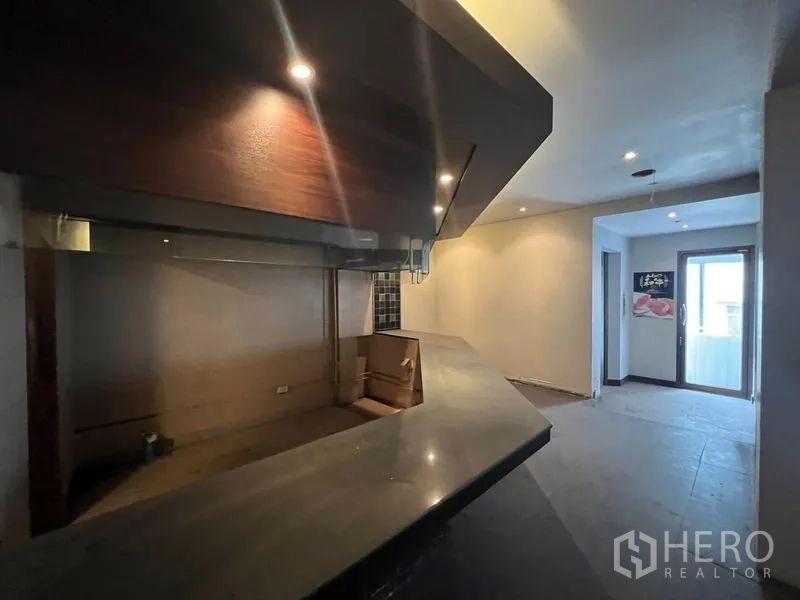 Shophouse for sale in Bang Rak, Bangkok - Long bar counter with overhead lighting connecting to a doorway to the balcony.