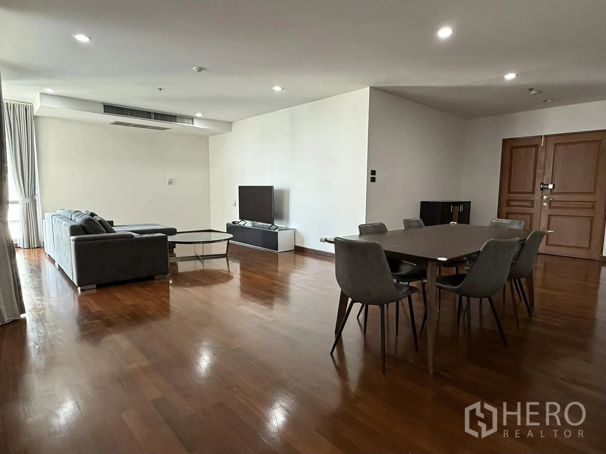 Condominium for rent in Pathum Wan, Bangkok - Spacious open-plan living and dining room with sofa, TV, and dining set.