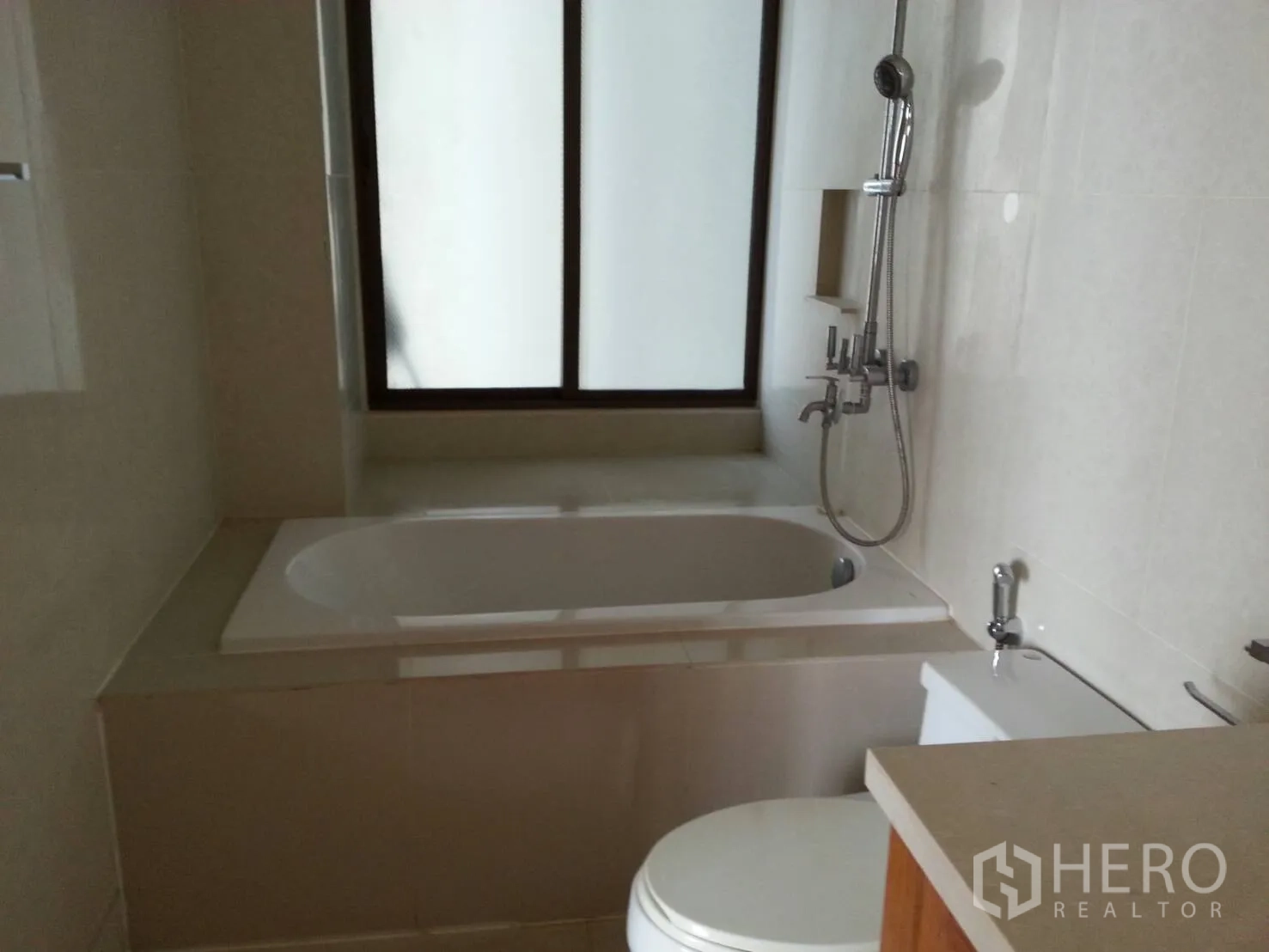 Condominium for rent in Khlong Toei, Bangkok - Modern bathroom featuring bathtub with shower and a frosted window.