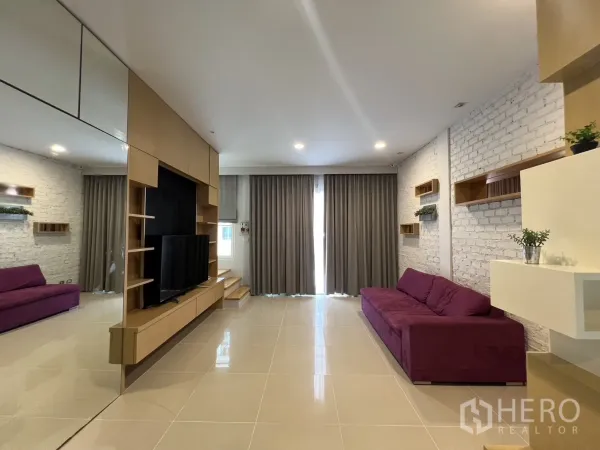 联排别墅 出租在Wang Thonglang, Bangkok - 宽敞起居室，双紫色沙发、整墙窗帘与搁架。
