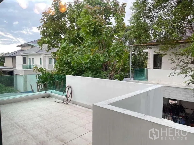 独立式住宅 出租在Mueang Nonthaburi, Nonthaburi - 楼上露台，玻璃栏杆与铺砖地面，眺望绿树。