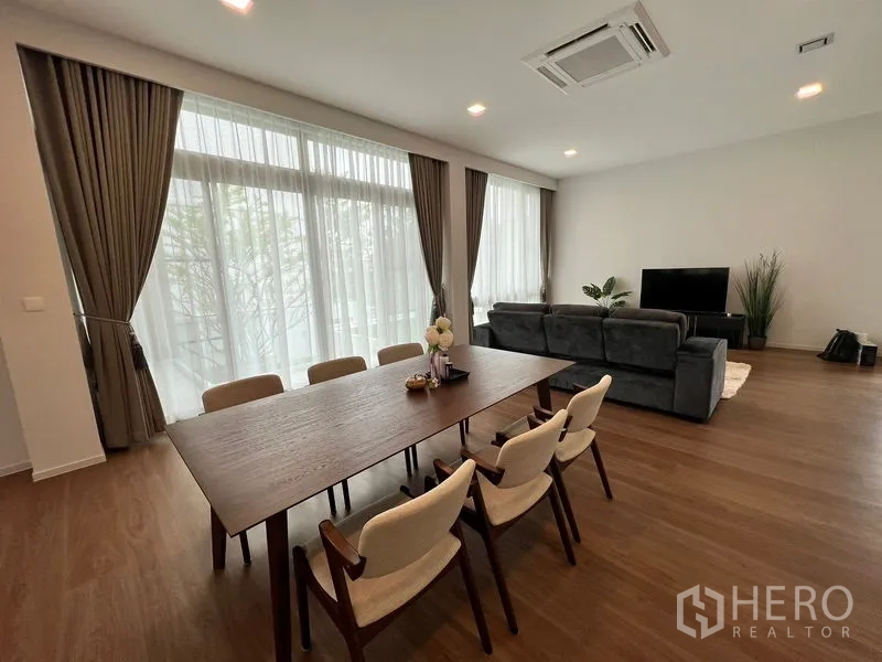 Detached House for rent or sale in Saphan Sung, Bangkok - Open‑plan dining area with six‑seat wooden table adjoining the lounge and large curtains.