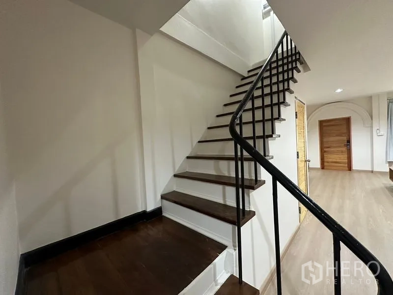 Townhouse for rent or sale in Phra Khanong, Bangkok - Close-up of wooden staircase with black metal handrail.