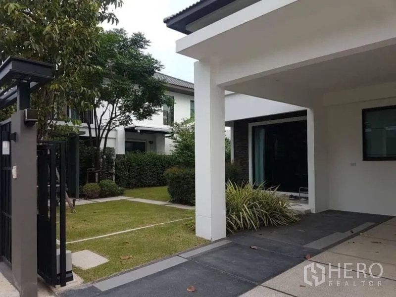 Detached House for rent in Bang Phli, Samut Prakan - Front gate and driveway leading to covered parking and landscaped yard.