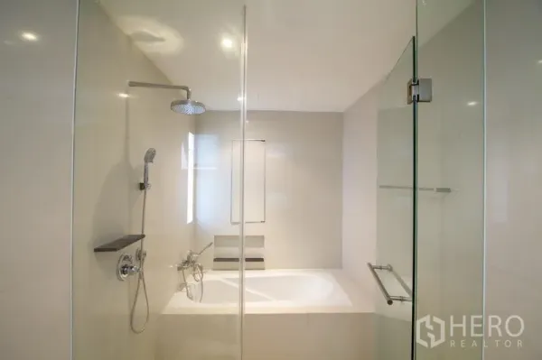 Apartment for rent in Watthana, Bangkok - Modern bathroom featuring a glass shower, separate bathtub, rain shower head, and neutral tiles.