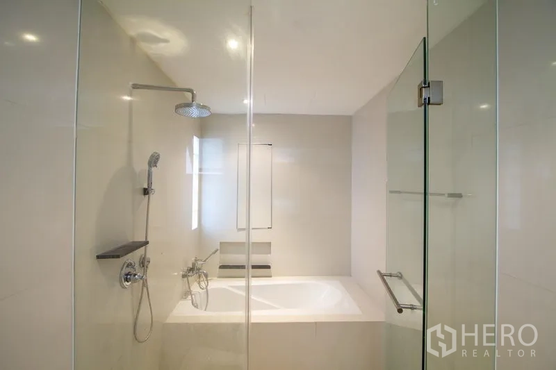 Apartment for rent in Watthana, Bangkok - Modern bathroom featuring a glass shower, separate bathtub, rain shower head, and neutral tiles.