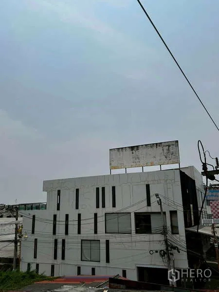 Home Office for rent or sale in Bang Phli, Samut Prakan - Side and rear view of the contemporary building with vertical windows and rooftop billboard structure.