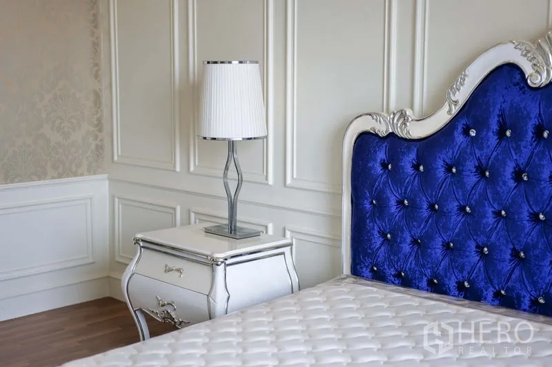 Condominium for rent in Khlong Toei, Bangkok - Primary bedroom detail featuring blue tufted headboard, nightstand, and paneled walls.