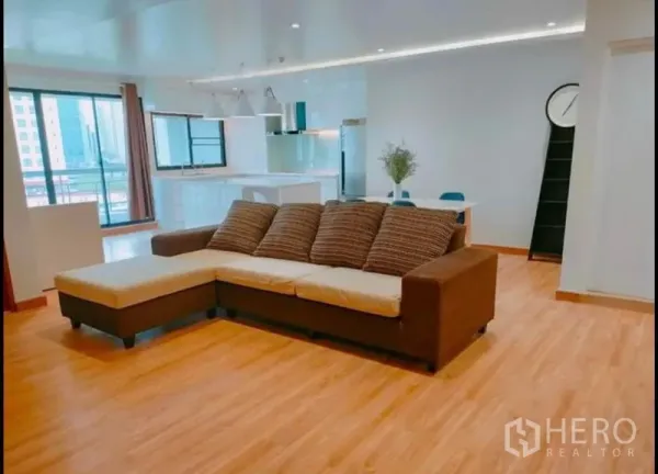 Condominium for sale in Watthana, Bangkok - Bright open-plan living room with L-shaped sofa, wood floors and balcony doors.