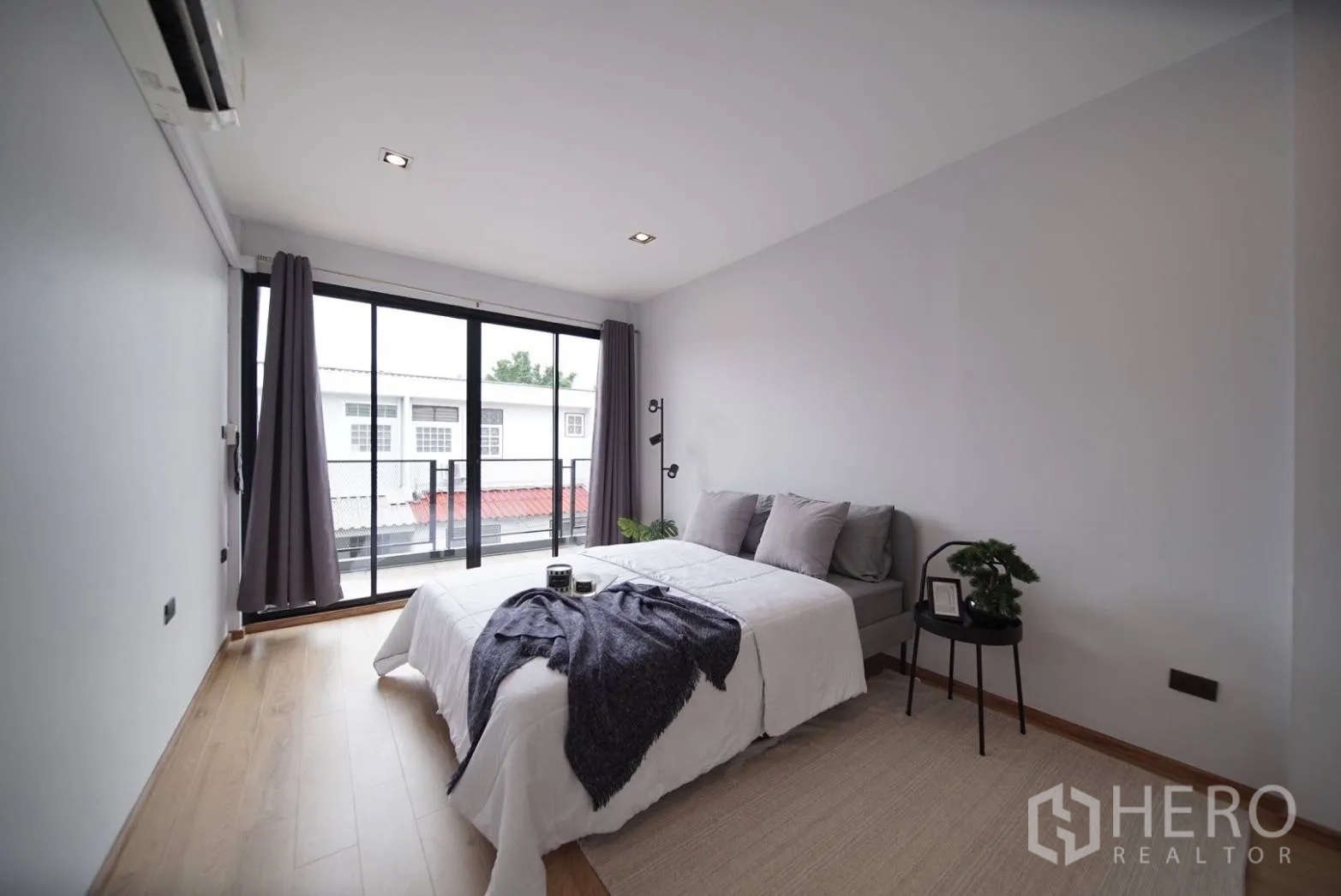 Townhouse for rent in Watthana, Bangkok - Bright bedroom with sliding glass doors to a balcony and wood flooring.