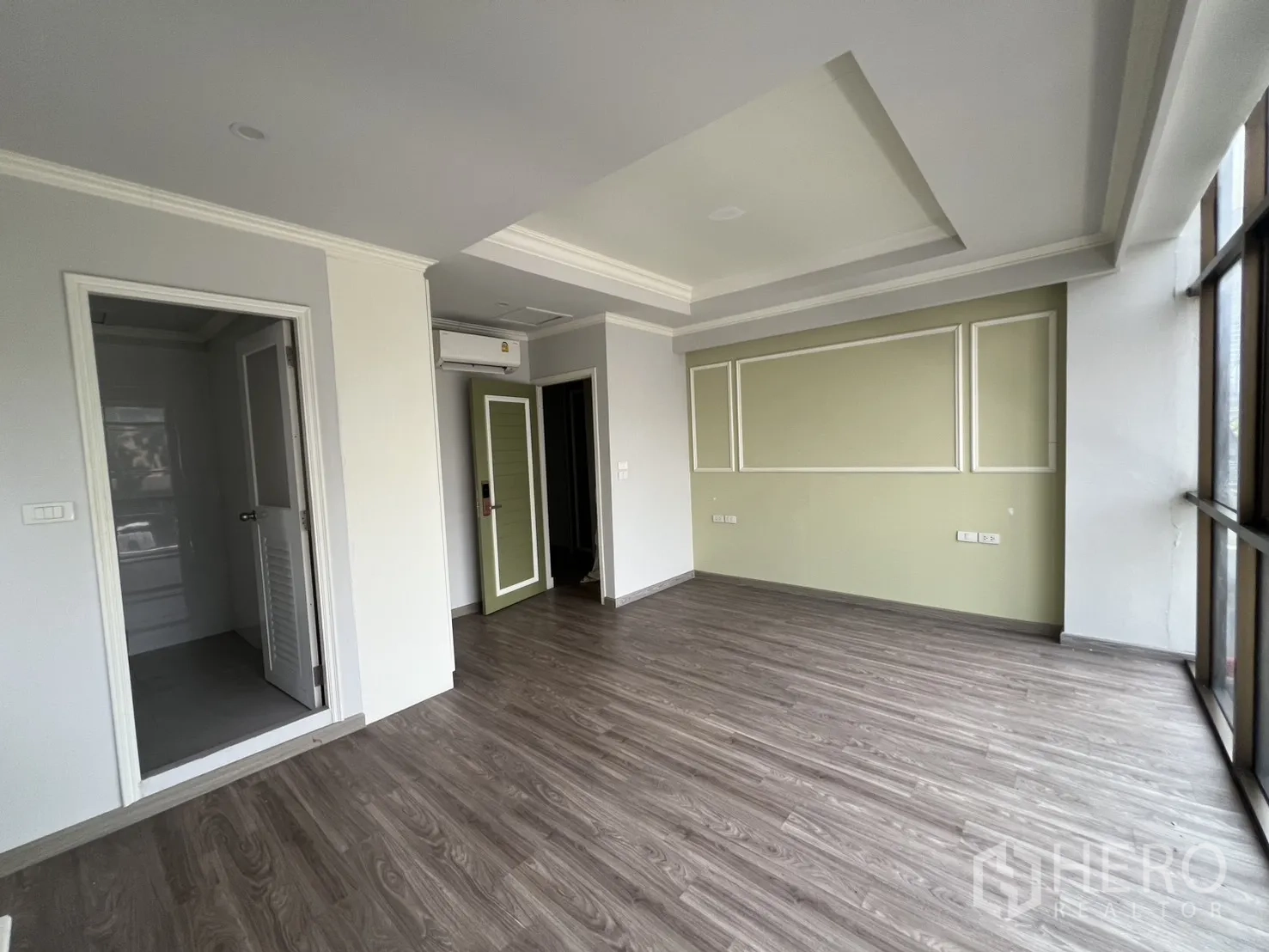 Shophouse for rent in Bang Rak, Bangkok - Bright upper-floor room with wood floors, green accent wall and wide windows.
