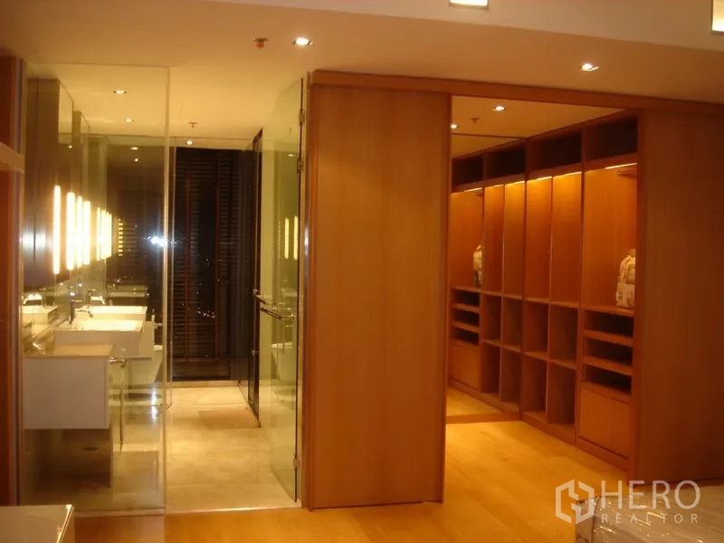 Condominium for rent in Sathon, Bangkok - Walk-in closet with illuminated wooden shelving beside a glass-walled bathroom.