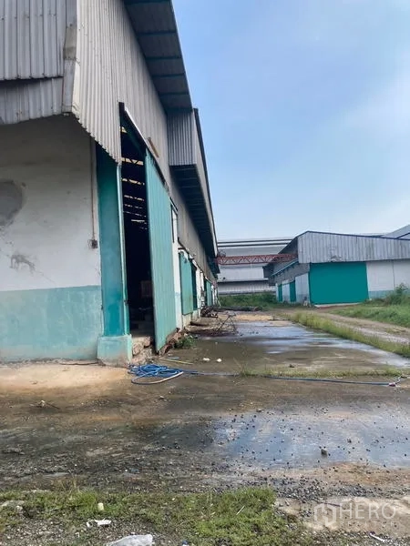 Warehouse for rent in Mueang Samut Sakhon, Samut Sakhon - Side service lane along a corrugated metal warehouse with drainage and access path.