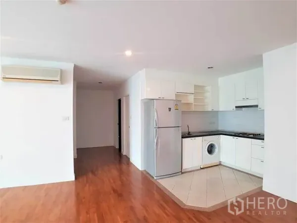 Condominium for rent in Sathon, Bangkok - Open-plan living and kitchen zone with wood floors, white cabinetry and air conditioning.