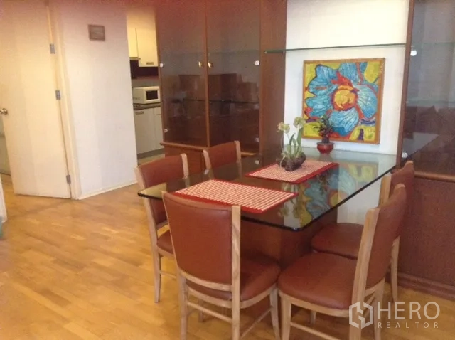Condominium for rent or sale in Din Daeng, Bangkok - Dining area with a glass-top table, six brown chairs, wood flooring, and colorful wall art in a Bangkok condo.