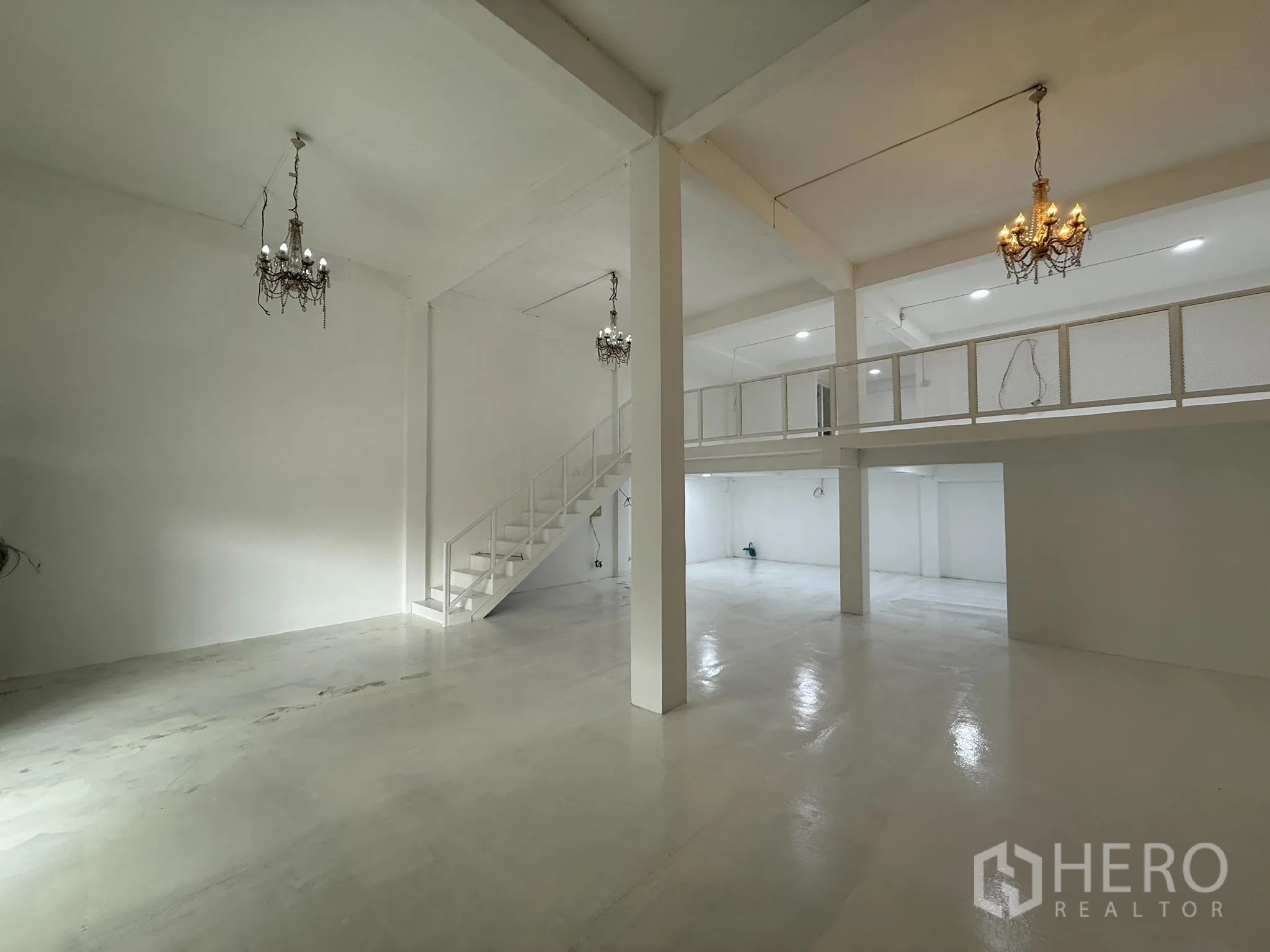 Shophouse for rent in Khlong Toei, Bangkok - Renovated open-plan white showroom with mezzanine and chandeliers.