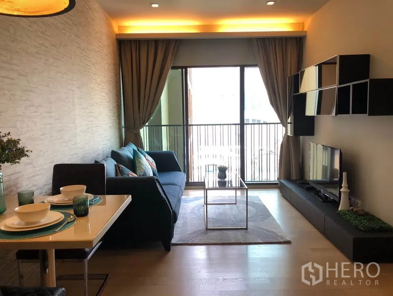 Condominium for rent in Bangkok - Bright living-dining area with floor-to-ceiling balcony doors, wall shelving, TV cabinet, and dining set.
