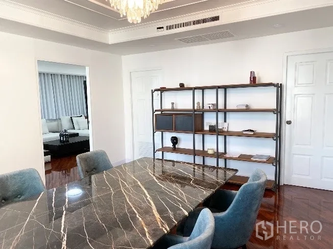 Condominium for rent in Khlong Toei, Bangkok - Elegant dining area with marble-top table, blue upholstered chairs and open shelving under a decorative ceiling.