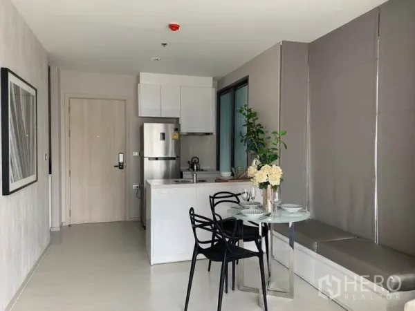 Condominium for rent in Khlong Toei, Bangkok - Compact modern kitchen with white cabinetry, island sink, stainless fridge, and a round dining table.