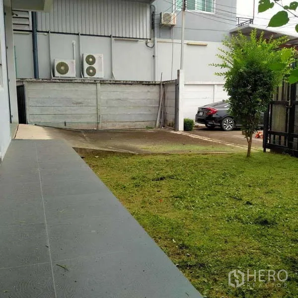 Factory for rent or sale in Ban Phaeo, Samut Sakhon - Side yard with grass lawn, driveway and outdoor AC units beside the building