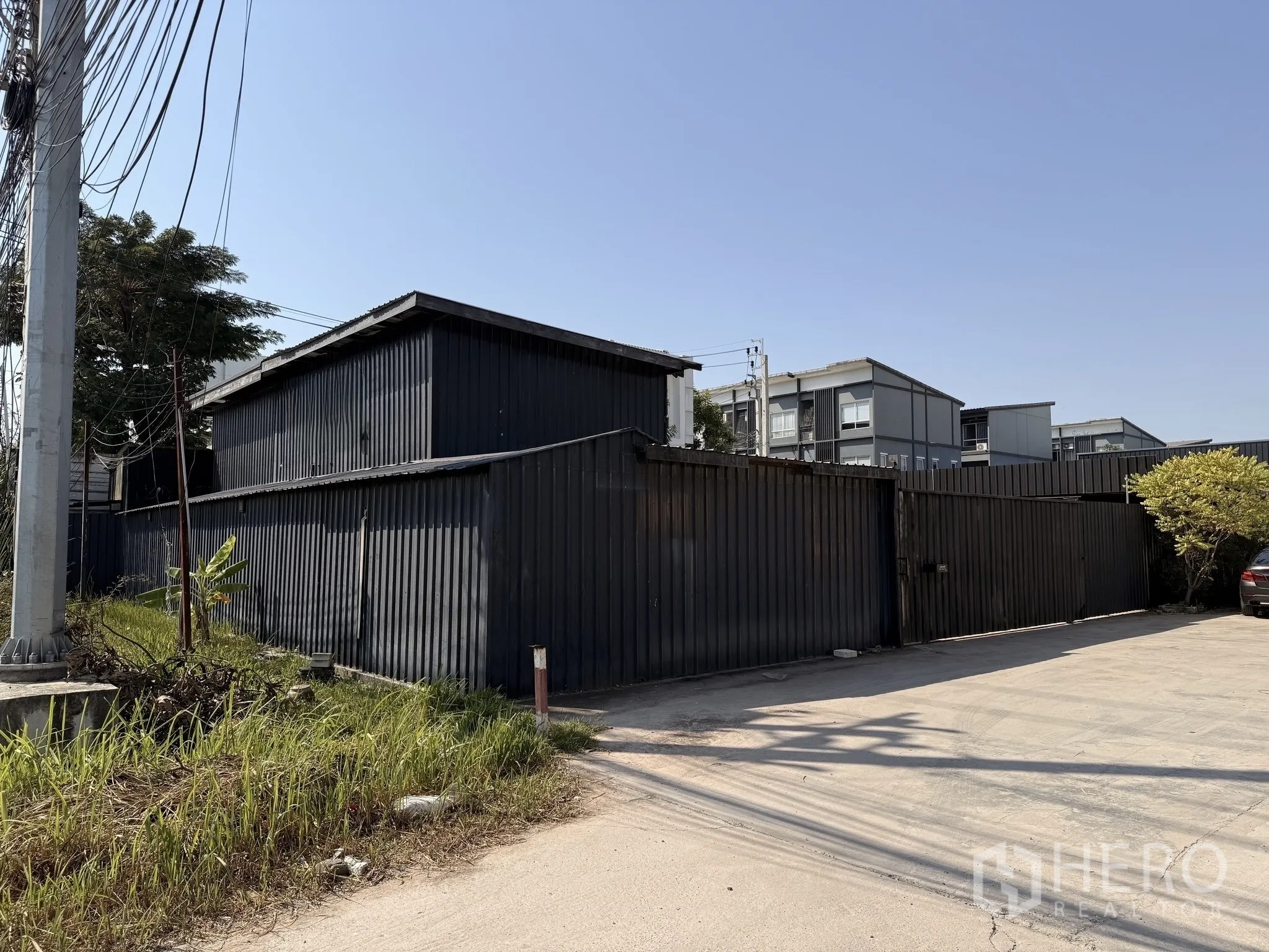 คลังสินค้า for rent in Lat Krabang, Bangkok - ภาพด้านหน้าคอมพาวด์โกดังเมทัลชีทสีดำ พร้อมทางเข้าและถนนกว้างในเขตประเวศ กรุงเทพฯ