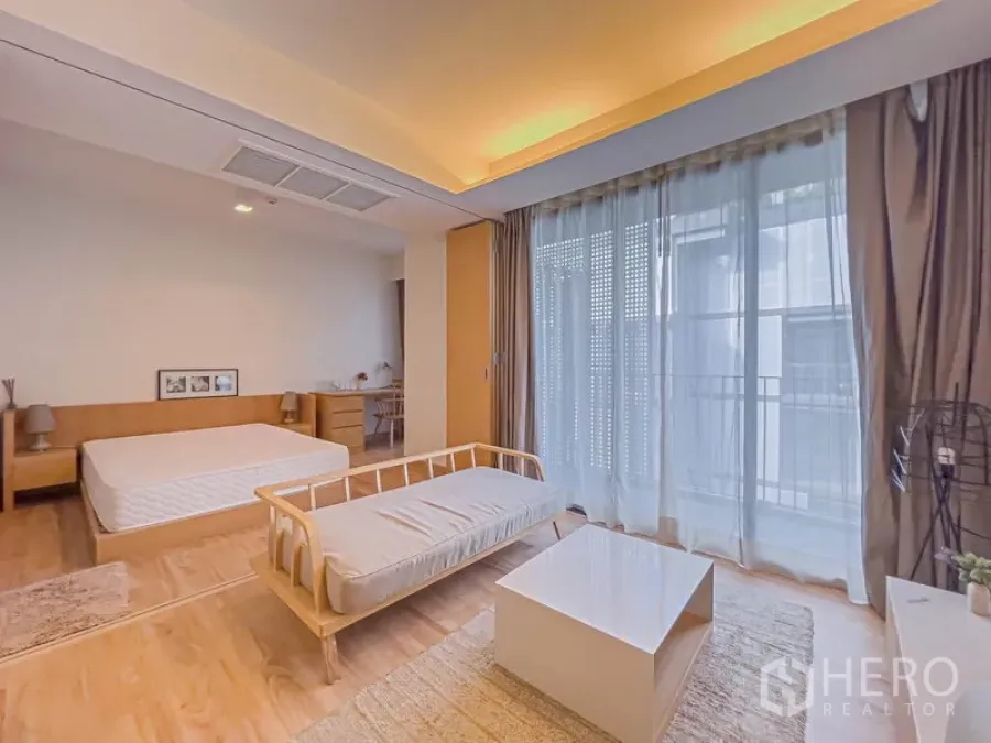 公寓 出售在Watthana, Bangkok - 采光充足的开放式起居与睡眠区，落地窗、暖色吊顶灯、沙发与床铺，木地板。