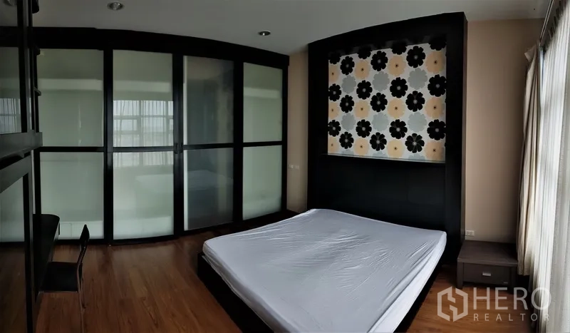 คอนโด ให้เช่าในRatchathewi, Bangkok - ห้องนอนพื้นไม้ ผนังหัวเตียงลายดอกไม้ พร้อมตู้เสื้อผ้าบานเลื่อนกระจกฝ้าและหน้าต่างผ้าม่านเต็มสูง