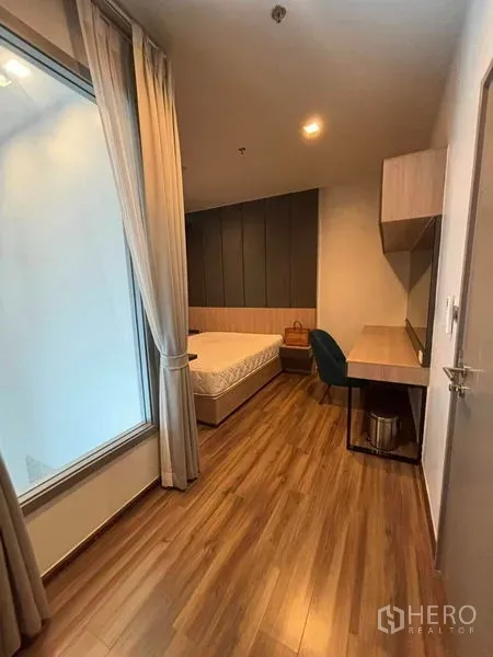 Condominium for rent or sale in Watthana, Bangkok - Second bedroom with large desk, shelving and wood floors beside an interior window.