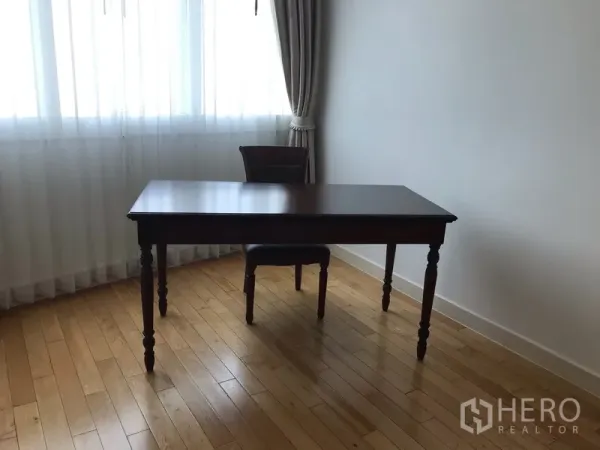 Condominium for rent in Khlong Toei, Bangkok - Sunlit study corner with wooden desk and chair beside a curtained window.